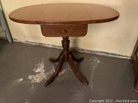 Perspective view of drop leaf table showing extended leaves, single drawer, and overall shape.
