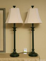 Full view of the pair of black candlestick table lamps with fabric shades on a flat surface against a beige wall.