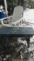 White wooden Muskoka chair next to blue wooden table on outdoor patio with snow patches