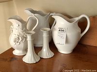 Three white pottery pitchers and a pair of white Limoges candlesticks arranged on a wooden surface.