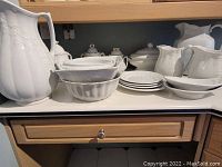 Wide view of counter holding white ceramic pitchers, tureen, bowls, and covered jars.