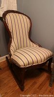 Full view of the rocking chair showing the upholstered striped fabric seat and backrest with carved wooden frame and rockers.