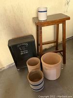 Photo showing all items together: wooden saddle stool, Jack Daniels box on casters, and four crocks.