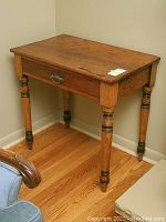Side view of vintage wooden side table showing turned legs and drawer handle.