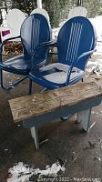 Two blue vintage metal chairs with snow on seats and weathered paint next to wooden bench with natural wood seat and gray painted base