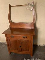 Front view of antique wooden wash stand showing single drawer with metal handles and two paneled cabinet doors below, curved wooden supports with horizontal rail above.