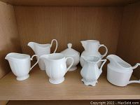 Shelf image showing a set of white ceramic creamers and sugar bowls of various brands and styles.