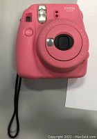Front view of flamingo pink Instax Mini 9 camera with lens, shutter button, and wrist strap visible.