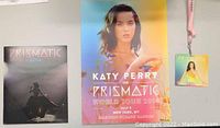 Photo showing poster with Katy Perry and related Prismatic Tour merchandise including badge and picture booklet.