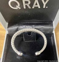 Front view of silver-tone braided open cuff wellness bracelet inside the black cushioned Q Ray box.