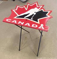 Photo of the folding tray table showing maple leaf shape, hockey player silhouette, and 'CANADA' text from an angle