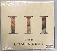 Front cover of The Lumineers III album showing beige cover with Roman numeral cutouts and band name, still shrink-wrapped