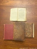 Three antique books laid out on wood surface: top opened French Robinson Crusoe book showing title page, bottom row with Holy Bible and Wuthering Heights closed.