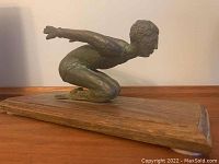 Side view of bronze diver sculpture showing crouched mid-dive pose and wooden base.