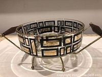 Side view of the glass chip and dip bowl within the metal holder showing the atomic geometric pattern and wooden handles.