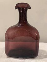 Front view of the large dark reddish-brown tinted glass water jug with a wide base and a single opening narrowing into double spouts at the top.