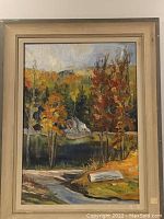 Full view of large framed landscape oil painting depicting a fall scene near water with trees and a bench.