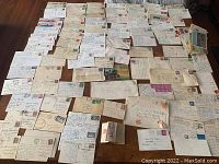 Table covered with numerous old postcards and envelopes, all featuring visible postage stamps and handwritten messages, displaying variety in type and age.