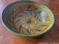 Side angle view of the pottery bowl showing floral painted décor and green rim against wooden surface.
