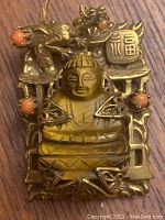 Front view of the brooch showing the detailed metalwork of the dragon and the tiger's eye Buddha centerpiece along with coral-colored beads