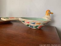 Side view of bird-shaped wooden scoop showing detailed hand-painted floral patterns and orange head with yellow beak.