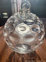Close-up of the clear glass witch ball showing raised circular patterns and bubble-like details on the surface.
