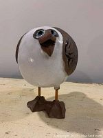 Frontal view of the terracotta seagull figurine showing the round body, white face, blue eyes, and brown beak with feet detail