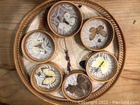 Top view of six round bamboo coasters with various butterfly illustrations arranged inside a round bamboo tray.