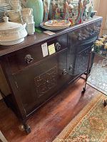 Front view of dark wood buffet showing two drawers, two cabinet doors with carved panels, bracket feet.