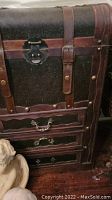 Close-up of one storage chest showing embossed pattern, leather straps with studs, latch closure, and drawers with metal handles.