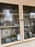 China and glassware displayed inside a glass cabinet with decorative plates, cups, and stemware visible.