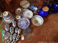 Birds eye view showing stacked plates and bowls with blue and white Asian inspired designs, along with two large blue ceramic pots and multiple small elephant-shaped pots.