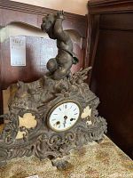 Front view showing the cherub figurine atop the iron mantle clock, ornate base, and clock face with Roman numerals