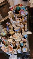 Overview of multiple ceramic figurines, vases, and decorative pots arranged on a dark wooden table.