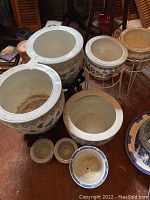 Top view of multiple ceramic planters in various sizes, mostly white with decorative rims and some with floral painted patterns, showing interior and exterior condition