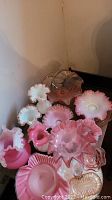 Multiple pink and white ruffled edge glass vases and bowls on table.