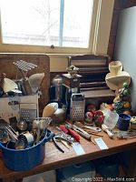Wide view of wooden table with assortment of vintage kitchen utensils including graters, hand beater, coffee grinder, kettle, and other metal and wooden tools.