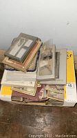 Top view of stacked picture frames including metal and wood frames, some in protective packaging.