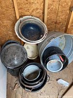 Top view of various metal pots and pans arranged in a pile, mostly round with some showing rust and dirt, including a black lid on one pot.