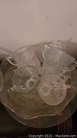 Top down view of a glass punch bowl containing five glass punch cups with handles, all placed on a large round matching glass serving tray.