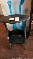 Front view of worn wooden side table showing kidney-shaped top and book storage compartment