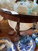 Full view of the round wood side table showing top, drawer, and pedestal base with three legs.