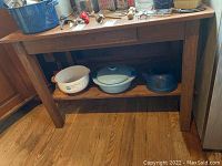 Front view showing entire wood table with items on top and underneath, wood grain and scratches visible.