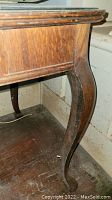 Close-up view of one curved and carved wooden leg of the side table, showing wood grain and wear.