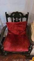 Front view of one vintage wood armchair with red velour cloth seat and carved wood backrest showing ornate cutout design and curved armrests.