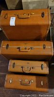 Four vintage brown leather suitcases stacked vertically showing different sizes and hardware details.