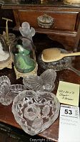 Selection of pressed glass trinket dishes and three porcelain figurines under glass domes on wooden surface