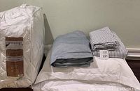 Photo showing the down alternative comforter in its packaging, along with the folded heather gray duvet cover and gray and white striped duvet set.