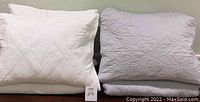 Two quilted shams, white on the left and gray on the right, showing detailed stitching patterns and filler pillows inside.