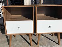 Front view showing two nightstands side by side, wood frame, white drawer fronts and tapered legs